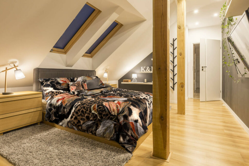 Łóżko pod skosem, na dalszym planie otwarte półki na ścianie prostopadłej do kolankowej