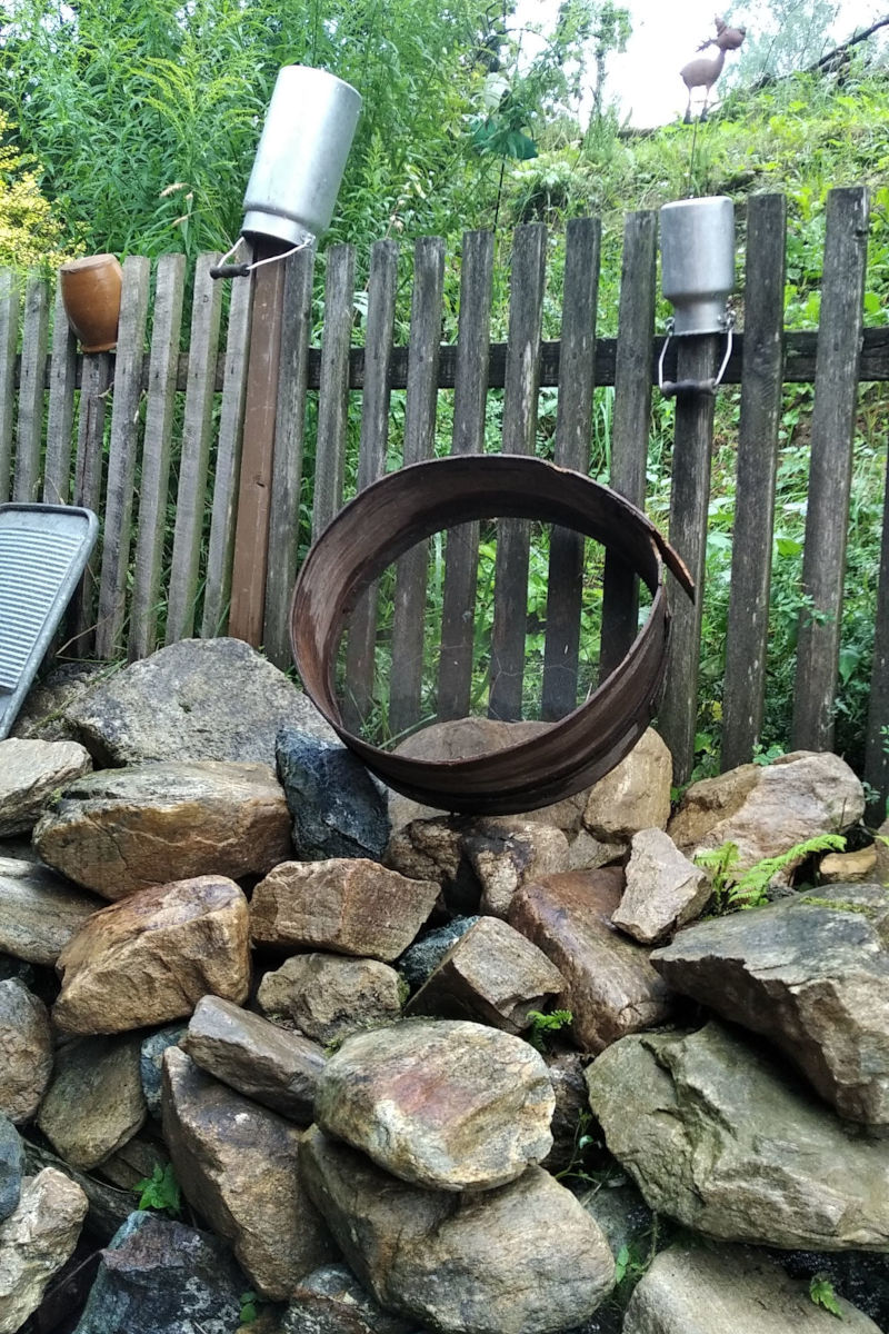 Drugie ujęcie drewnianego płotu z rustykalnymi ozdobami: kamionkowymi garnkami, kanką i metalowym sitem