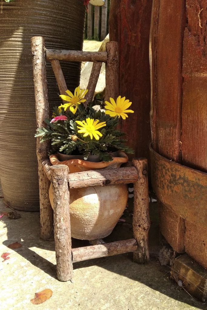 Oryginalny drewniany kwietnik w kształcie krzesełka z glinianą osłonką na doniczkę.