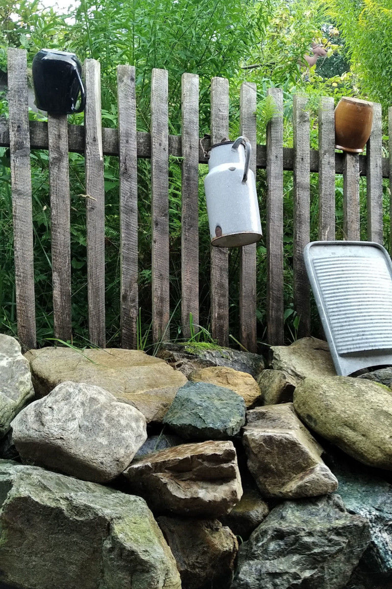 Drewniany płot z rustykalnymi ozdobami: kamionkowymi garnkami, kanką i tarą do prania.